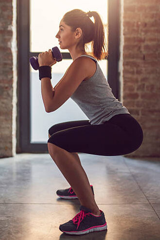 A young woman in Arlington doing bodyweight squats with dumbbell rows during her home workout.