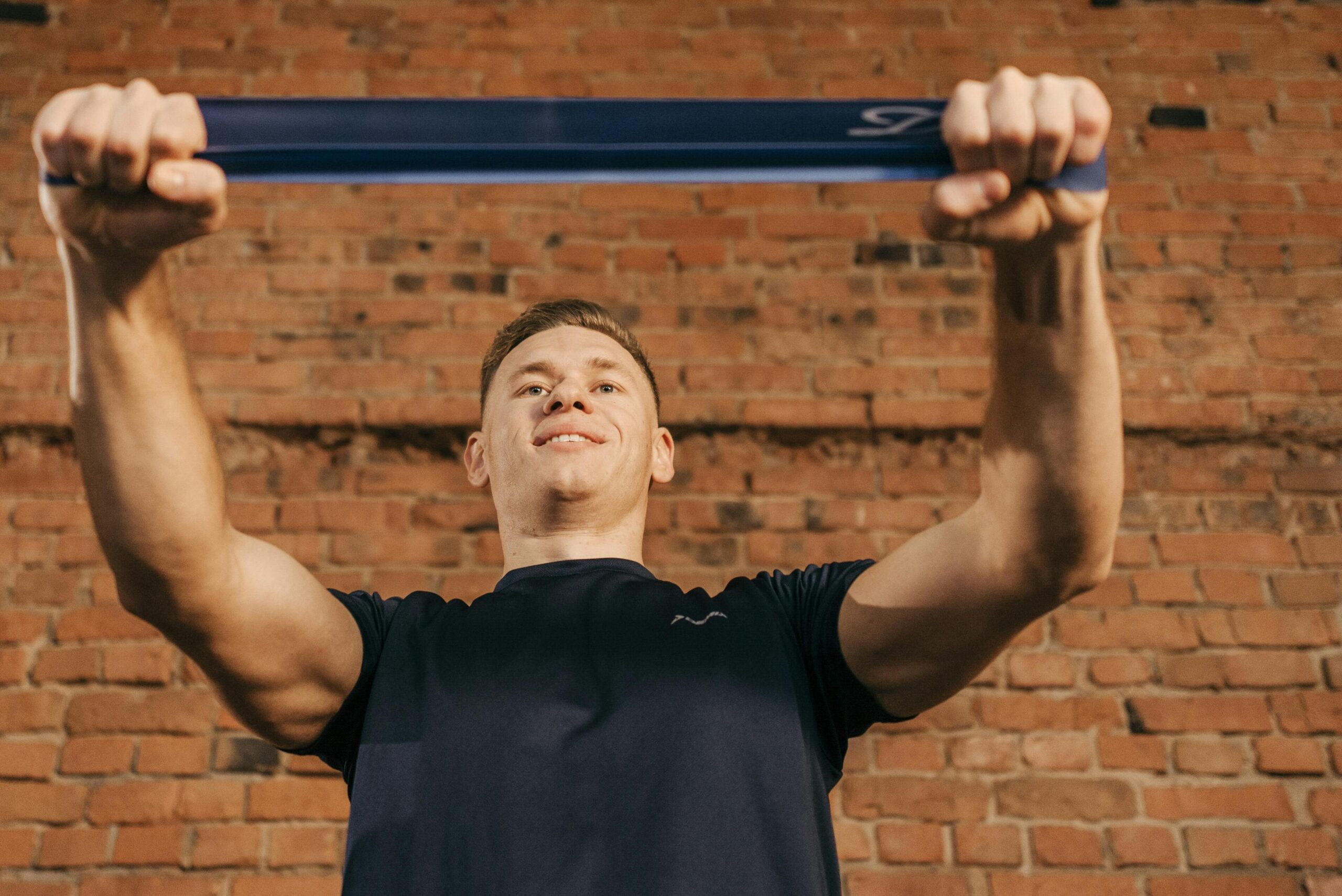 A young man pulling a resistance band during his home workout, incorporating bodyweight exercises and maintaining his fitness routine