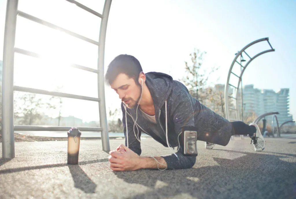 A young man performs a plank exercise outdoors with earphones, a phone, and a water bottle nearby.

Exercises You Should Do Every Day 