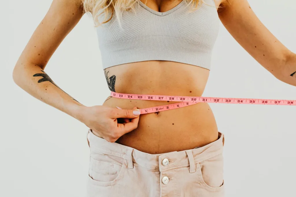 A close-up of an American woman measuring her waist, symbolizing weight loss success through healthy habits and exercise.