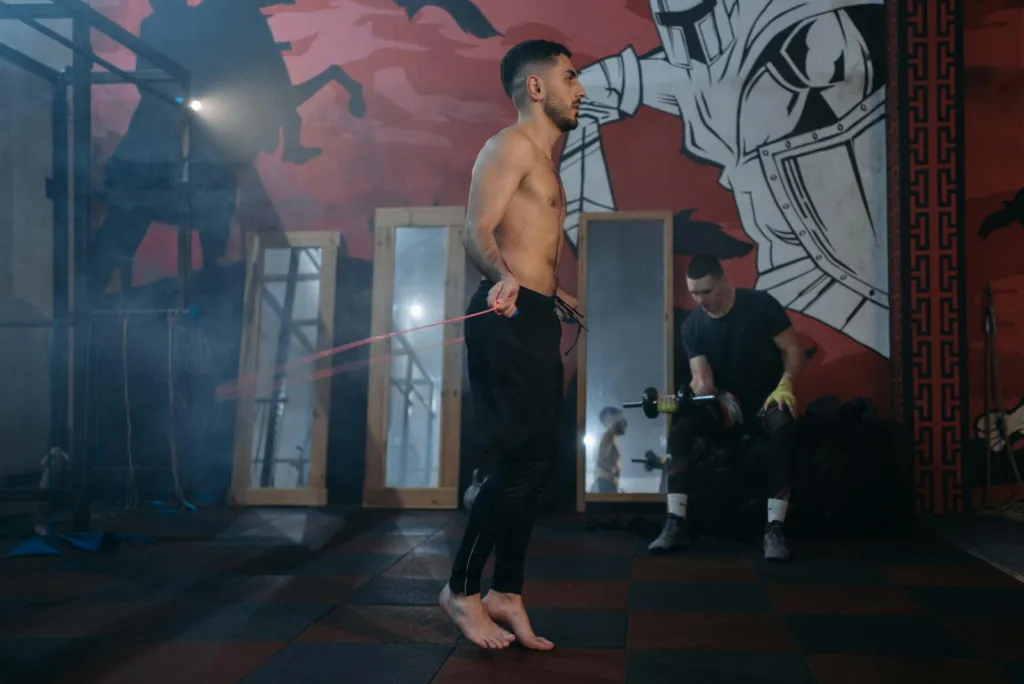 Shirtless man practicing jump rope in an urban gym with wall art.