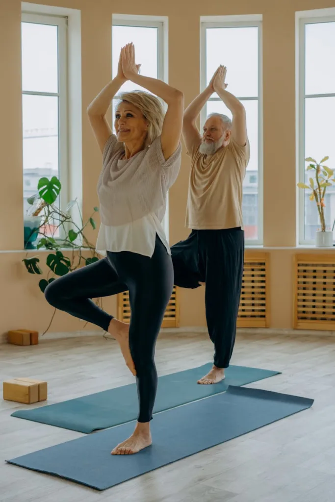 Elderly American couple practicing gentle exercises with yoga poses indoors, promoting wellness and mindfulness.