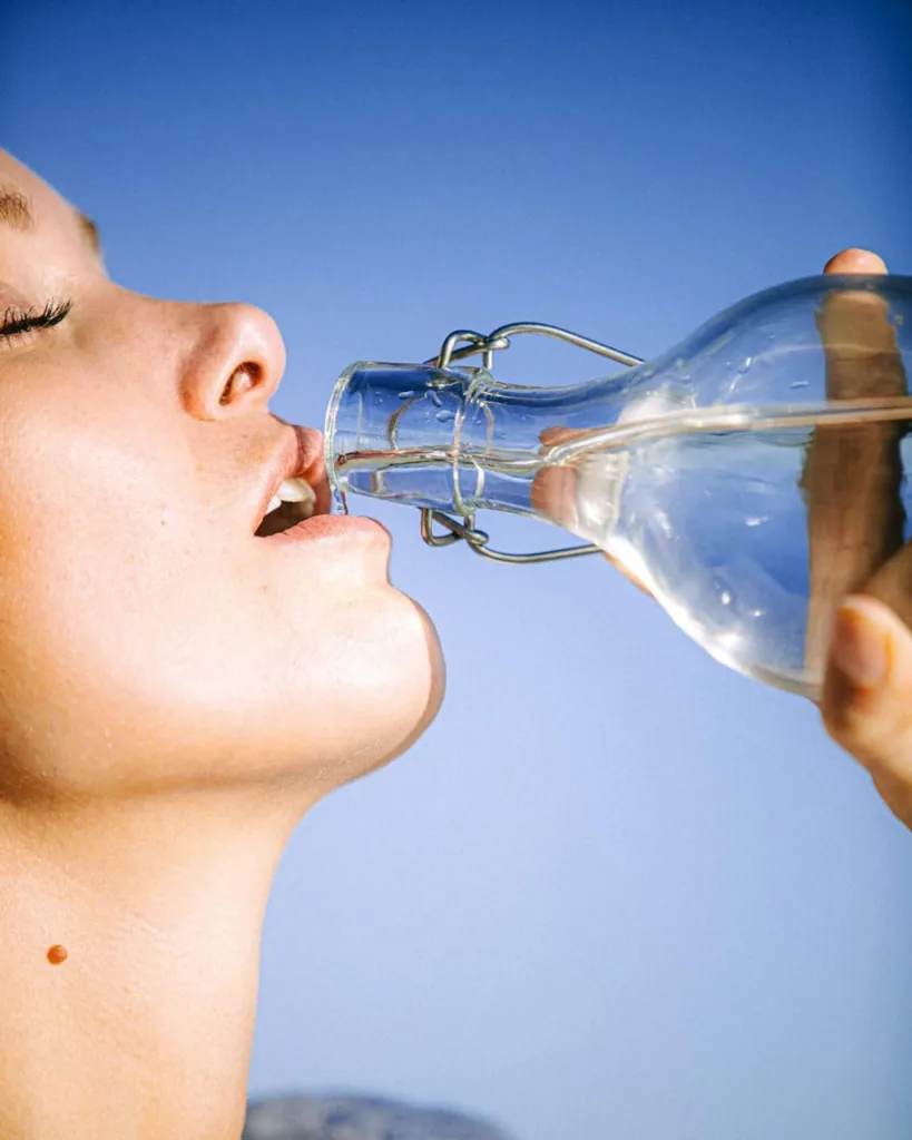 American woman drinking water to stay hydrated, a key factor in promoting healthy weight loss and burning belly fat.