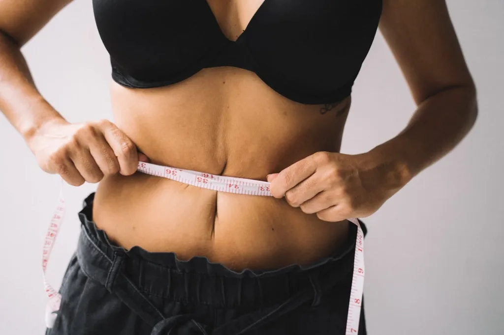 American person measuring their belly size to track progress in losing belly fat and achieving fitness goals.