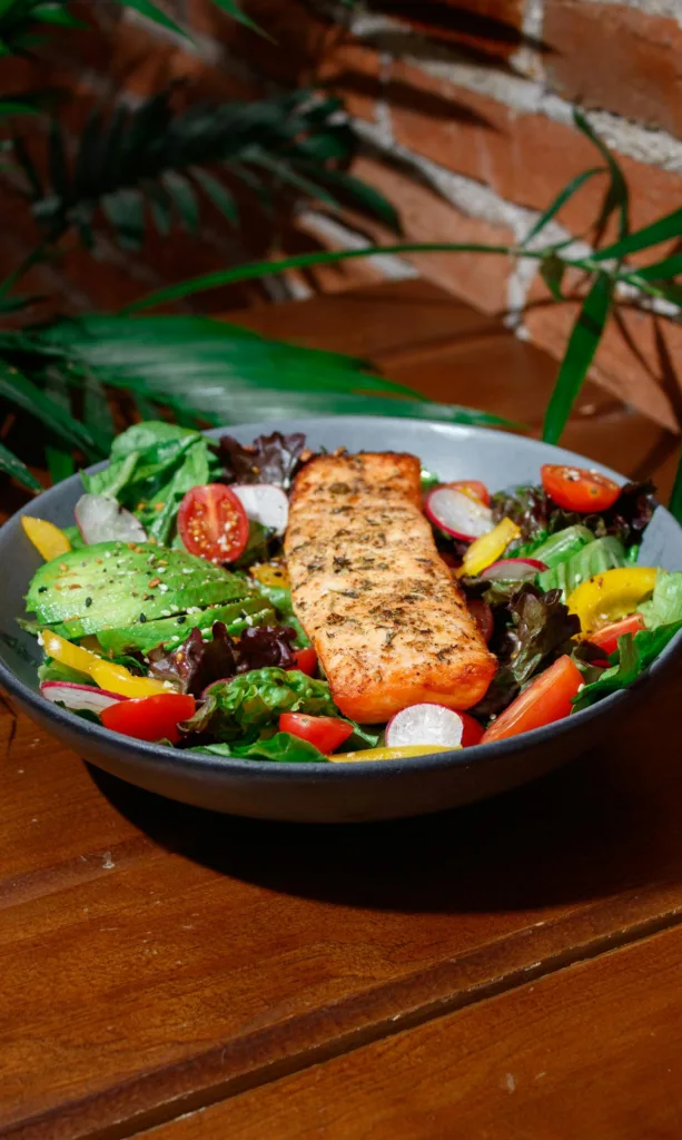 A healthy meal with grilled salmon, rich in Protein and Omega 3 Fatty Acids, served on a bed of fresh greens and colorful vegetables, ideal for senior fitness and Americans looking to improve their nutrition.