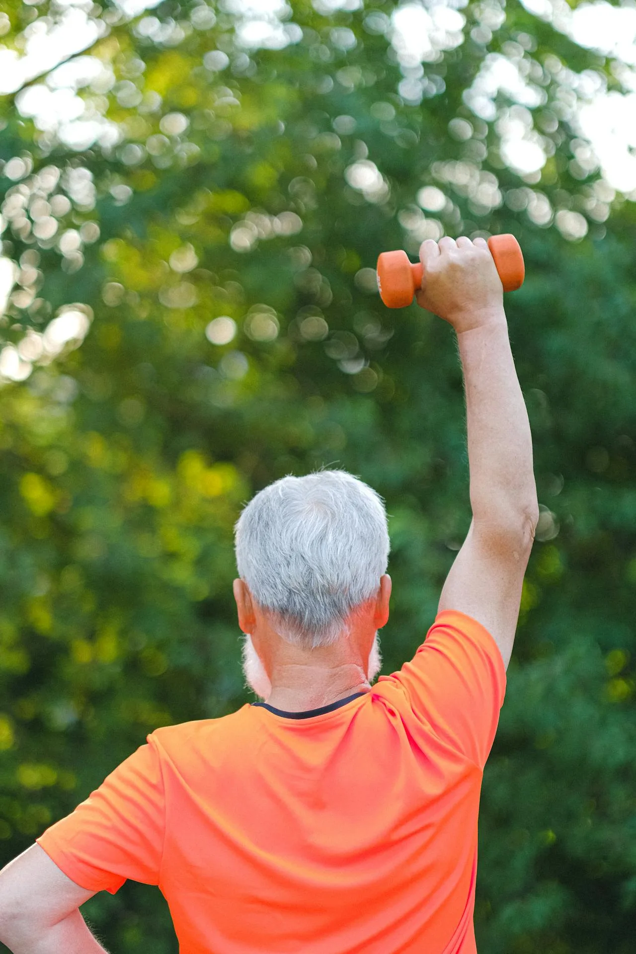 Senior man lifting a dumbbell in a green, natural outdoor setting, showcasing American fitness for seniors in a healthy and active lifestyle.