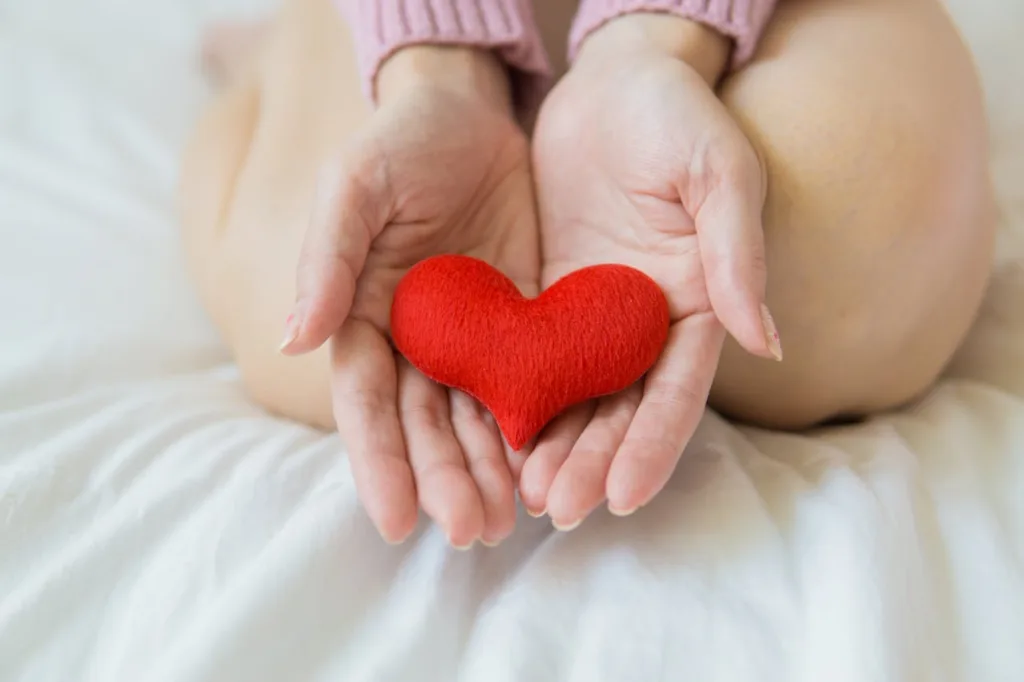 Two hands gently holding a red felt heart, symbolizing love and care, representing a healthy lifestyle and the importance of self-care through exercise and wellness in Americans.