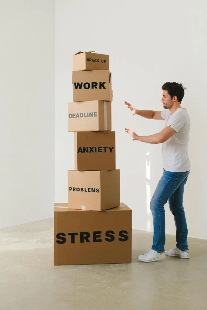 A person standing next to a stack of boxes labeled with "Stress," "Problems," "Anxiety," "Deadline," and more, illustrating the impact of stress on mental health and how a healthy lifestyle and regular exercise can help manage it in America.