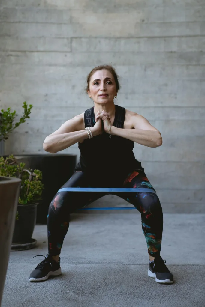 Older woman performing squats indoors with the help of a resistance band, demonstrating gentle exercises to stay active and fit.